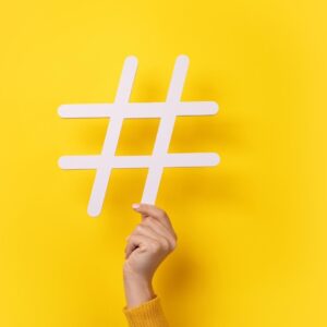 A hand holding a hashtag with a yellow background - we discuss everything you need to know about hashtags in social media